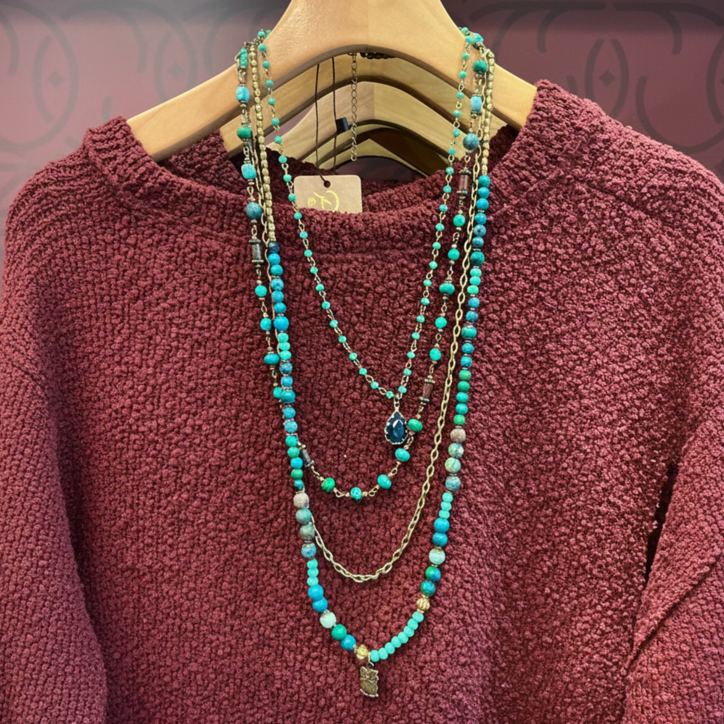 Turquoise beaded necklace on a hanger against a maroon sweater
