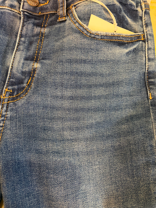 Vervet Masterfully Jean jeans hanging on a wooden background, featuring classic denim style and detailed stitching.