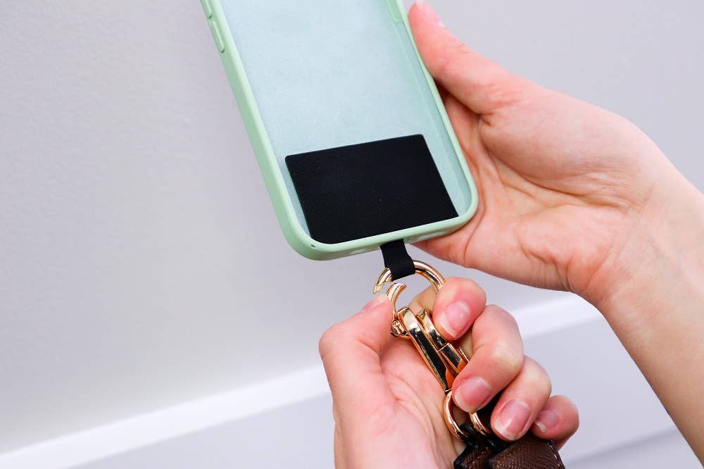 Save The Girls Clip & Go crossbody phone strap with stylish chain and clip design, attached to a smartphone for hands-free convenience.