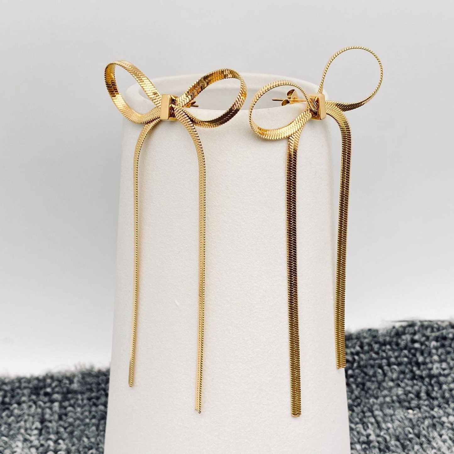 Mio Queena chain bow earrings featuring delicate gold-tone chains and bow charms, stylish and elegant jewelry accessory