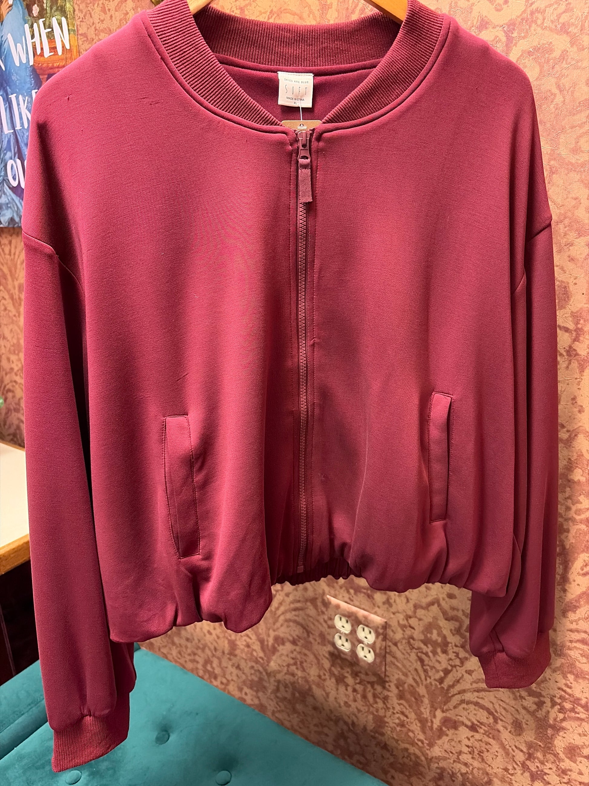 Skies Are Blue Rosewood Bomber Jacket shown in black with a zip front and ribbed cuffs, displayed on a hanger.