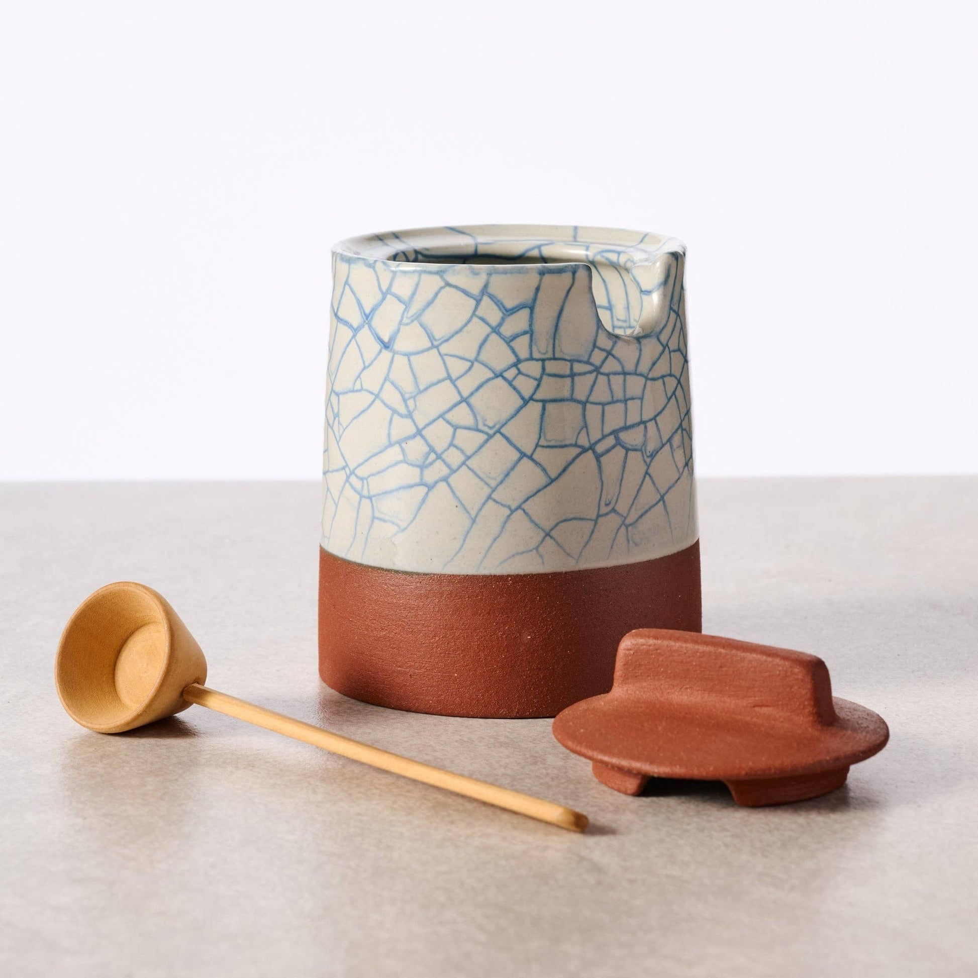 Ciya Blue Crackle Honey Pot by Ten Thousand Villages, ceramic honey jar with a blue crackle glaze and lid on a wooden surface.