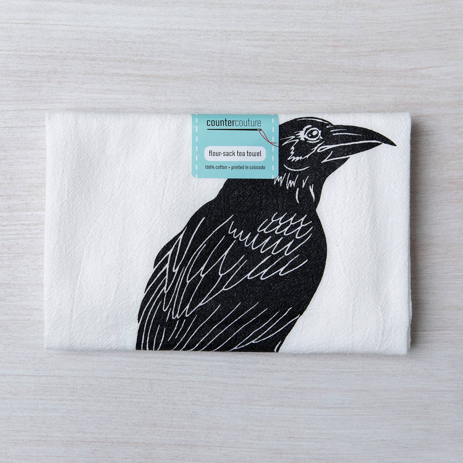 Counter Couture Raven tea towel with screen-printed design, made in USA, displayed hanging in a kitchen setting.