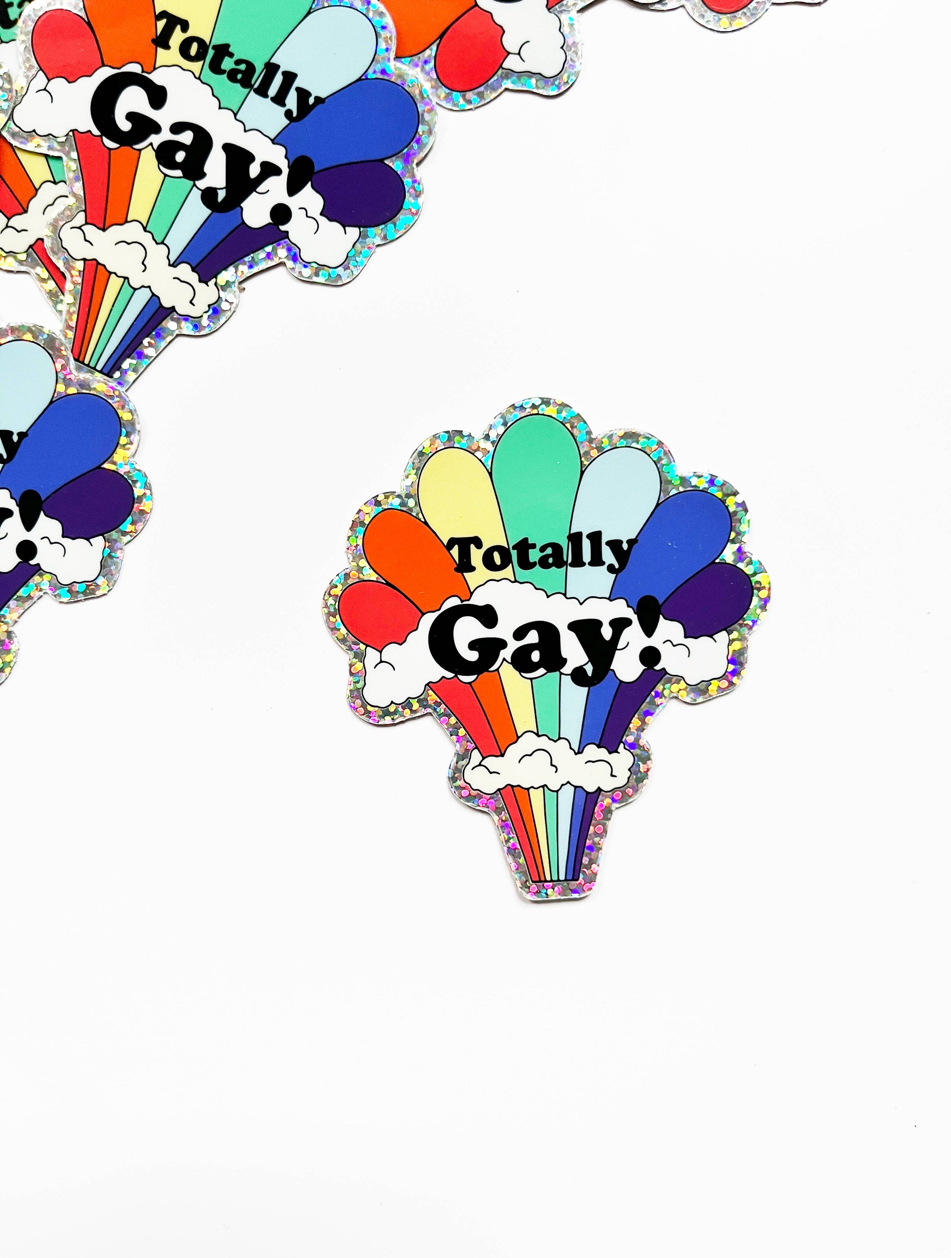 Colorful rainbow glitter sticker featuring the "Totally Gay" design by The Coin Laundry, perfect for decorating laptops and water bottles.