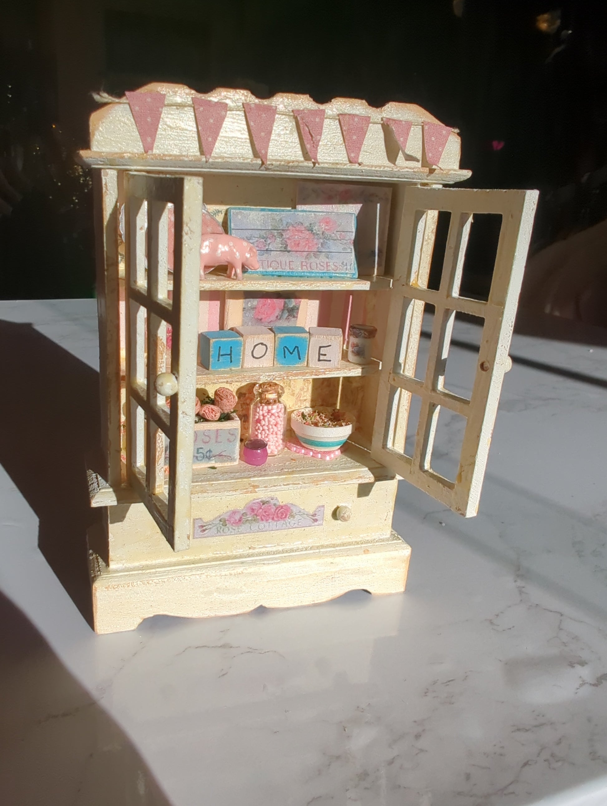 Miniature pink and white hutch scene from Detail In Miniature, featuring tiny furniture and decorative details in a miniature setting.